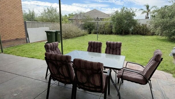 An outdoor patio with a table and six striped chairs, a covered area, and a view of a grassy yard and distant hills. - 2BR Seaside Retreat in Largs North (Largs North)