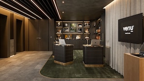 A modern hotel lobby with a reception desk, a flat-screen TV, and a wall decorated with various items. - Veriu Richmond (Richmond)