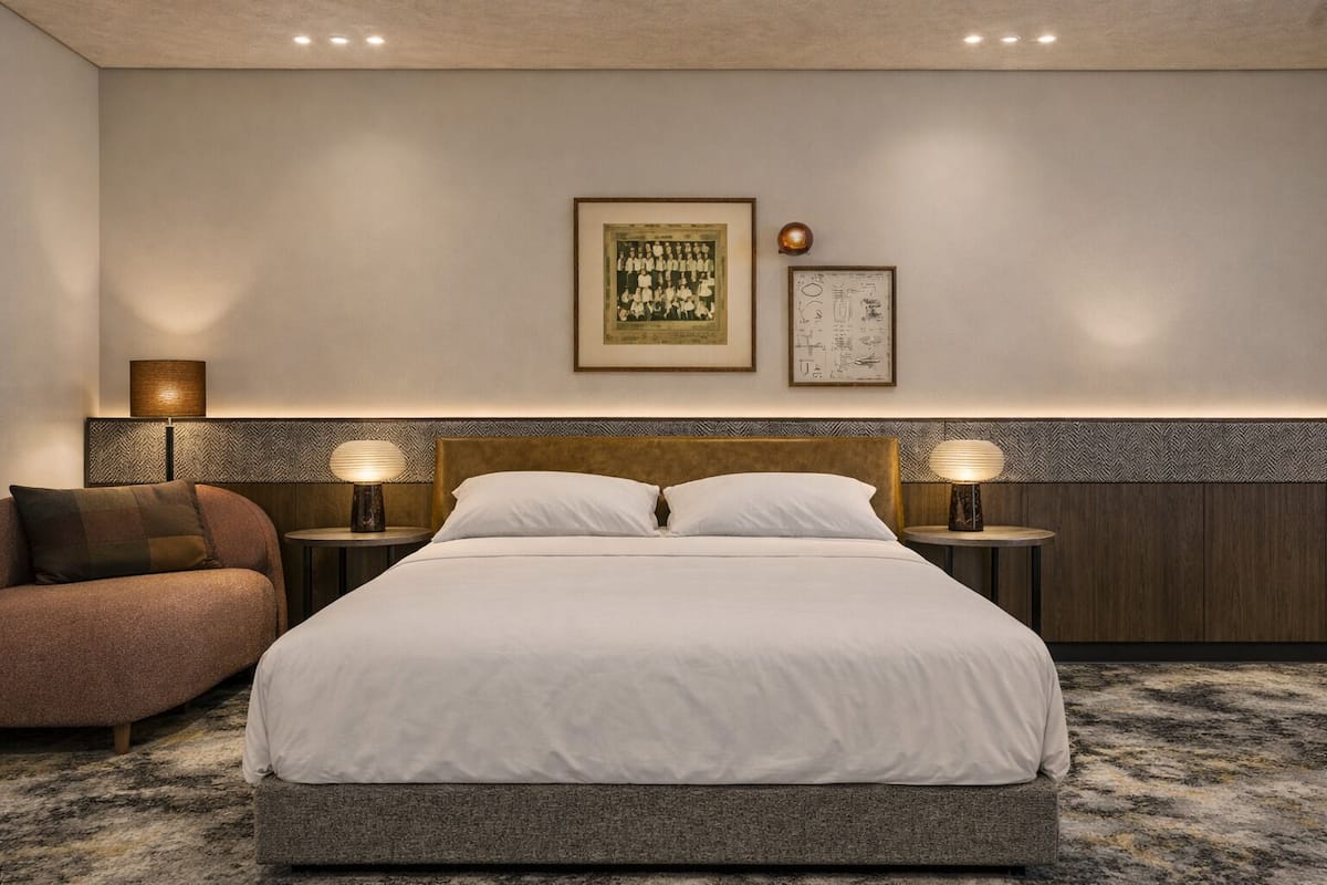 A hotel room with a large bed, two bedside tables with lamps, a sofa, and two framed pictures on the wall.