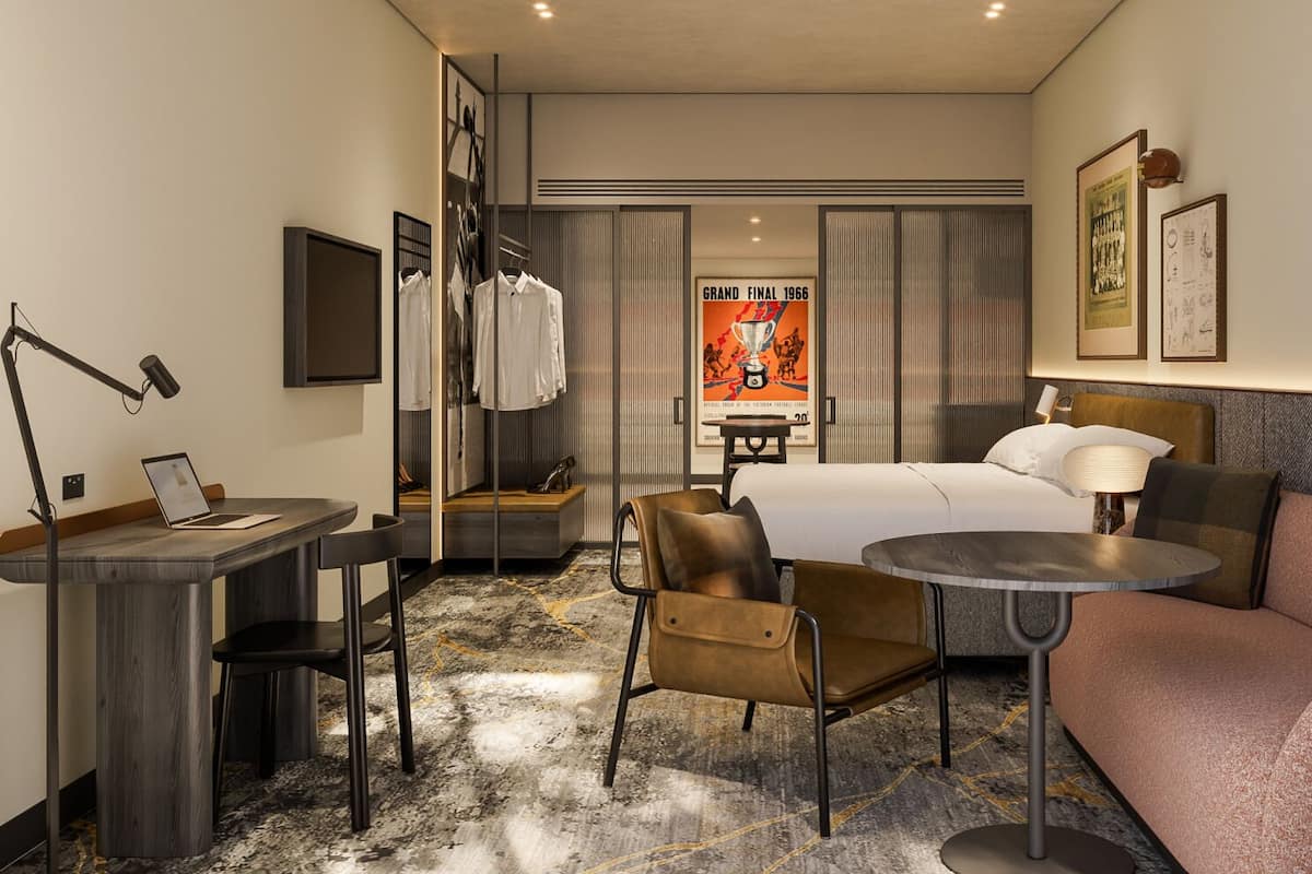 A hotel room with a bed, a sofa, a desk with a laptop, a chair, a small table, and a poster on the wall.