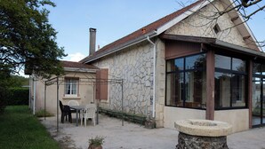 Ein Steinhhaus mit großem Fenster, Schornstein und kleinem Garten mit Tisch und Stühlen.