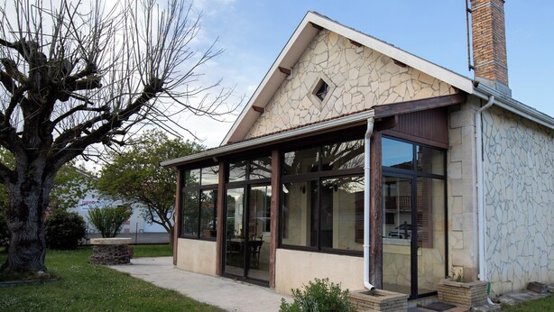 Ein modernes Haus mit Steinfassade, großen Glasfenstern und einer überdachten Terrasse.
