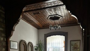 Uma sala de estar aconchegante com pé direito alto, uma janela grande com cortinas finas, um sofá, uma mesa de centro e um tapete estampado.