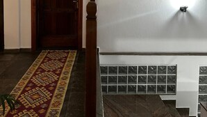 Um corredor com porta de madeira, tapete estampado, escada com corrimão branco e um quadro emoldurado na parede.