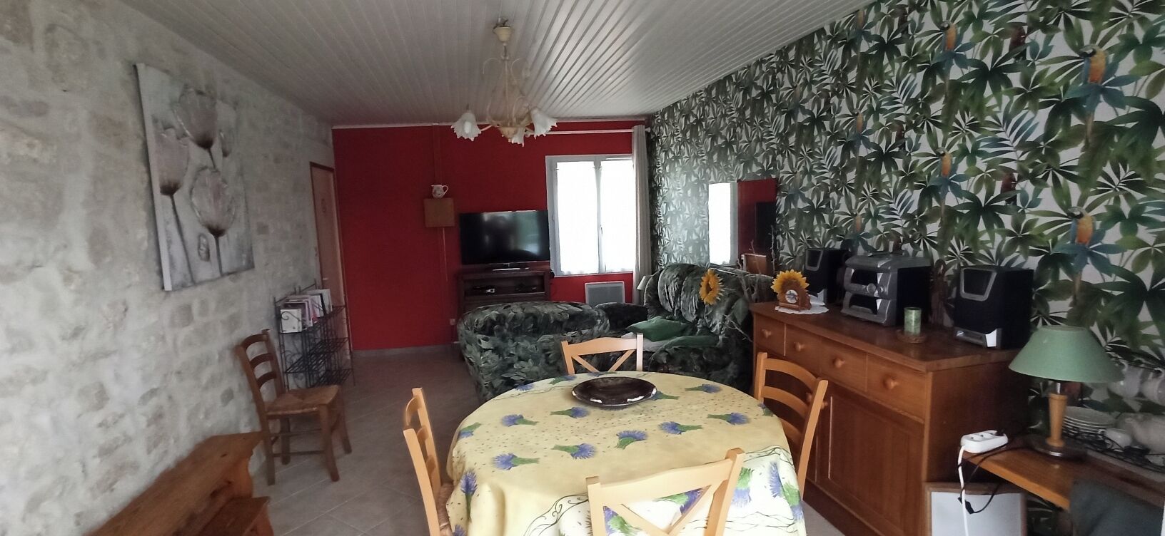 Une pièce comprenant une table à manger, des chaises, un téléviseur, un canapé et un mur décoré d’un motif.