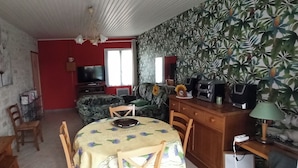 A room with a dining table, chairs, a television, a sofa, and a patterned wall. - Au Calme 4 star house 2 bedrooms large swimming pool 6x12 m sea and town 1,5 km (Saint-Pierre-d'Oléron)