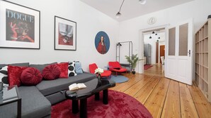A modern living room with a grey sofa, red cushions, a black coffee table, and a red rug. There are framed pictures on the wall, a red chair, and a floor lamp. - Elegant Apartment in the Center | Close to the Market, Place to Work (Wrocław)