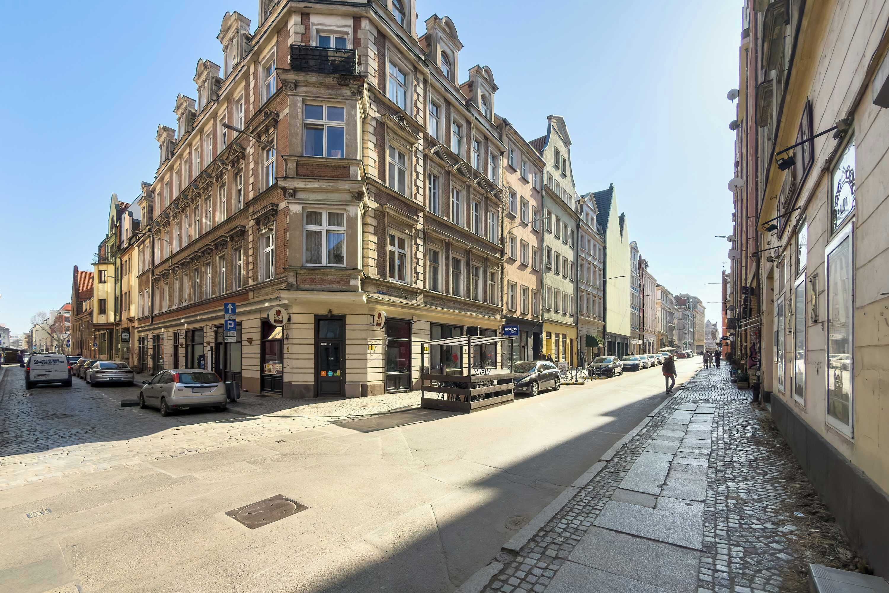 A street with historic buildings, a sidewalk, and parked cars.