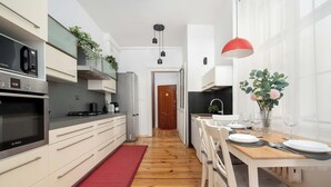 A modern kitchen with white cabinetry, a red rug, and a dining area with a wooden table set for four. - Elegant Apartment in the Center | Close to the Market, Place to Work (Wrocław)