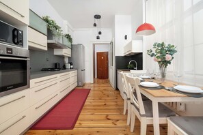 A modern kitchen with white cabinetry, a red rug, and a dining area with a wooden table set for four. - Elegant Apartment in the Center | Close to the Market, Place to Work (Wrocław)