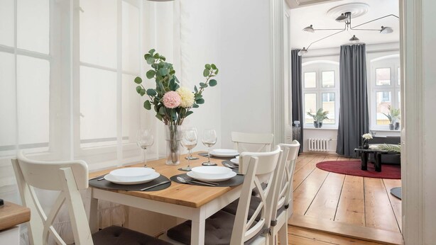 A dining area with a wooden table set for four, white chairs, and a vase of flowers. - Elegant Apartment in the Center | Close to the Market, Place to Work (Wrocław)
