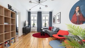 A modern living room with a wooden floor, a red sofa, a grey sofa, a red armchair, a black coffee table, a red rug, a bookshelf, and a large window with curtains. - Elegant Apartment in the Center | Close to the Market, Place to Work (Wrocław)