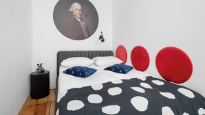 A bedroom with a grey headboard, a bed with white and blue pillows, a black side table, and a red accent pillow. - Elegant Apartment in the Center | Close to the Market, Place to Work (Wrocław)