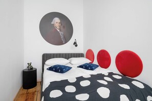 A bedroom with a grey headboard, a bed with white and blue pillows, a black side table, and a red accent pillow. - Elegant Apartment in the Center | Close to the Market, Place to Work (Wrocław)