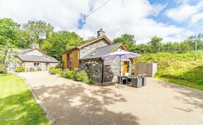 Une maison en pierre dotée d’un patio, d’une terrasse en bois et d’un espace salon couvert avec un parasol.