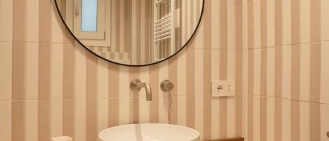 Un baño con un espejo redondo, un lavabo blanco y azulejos a rayas en la pared.