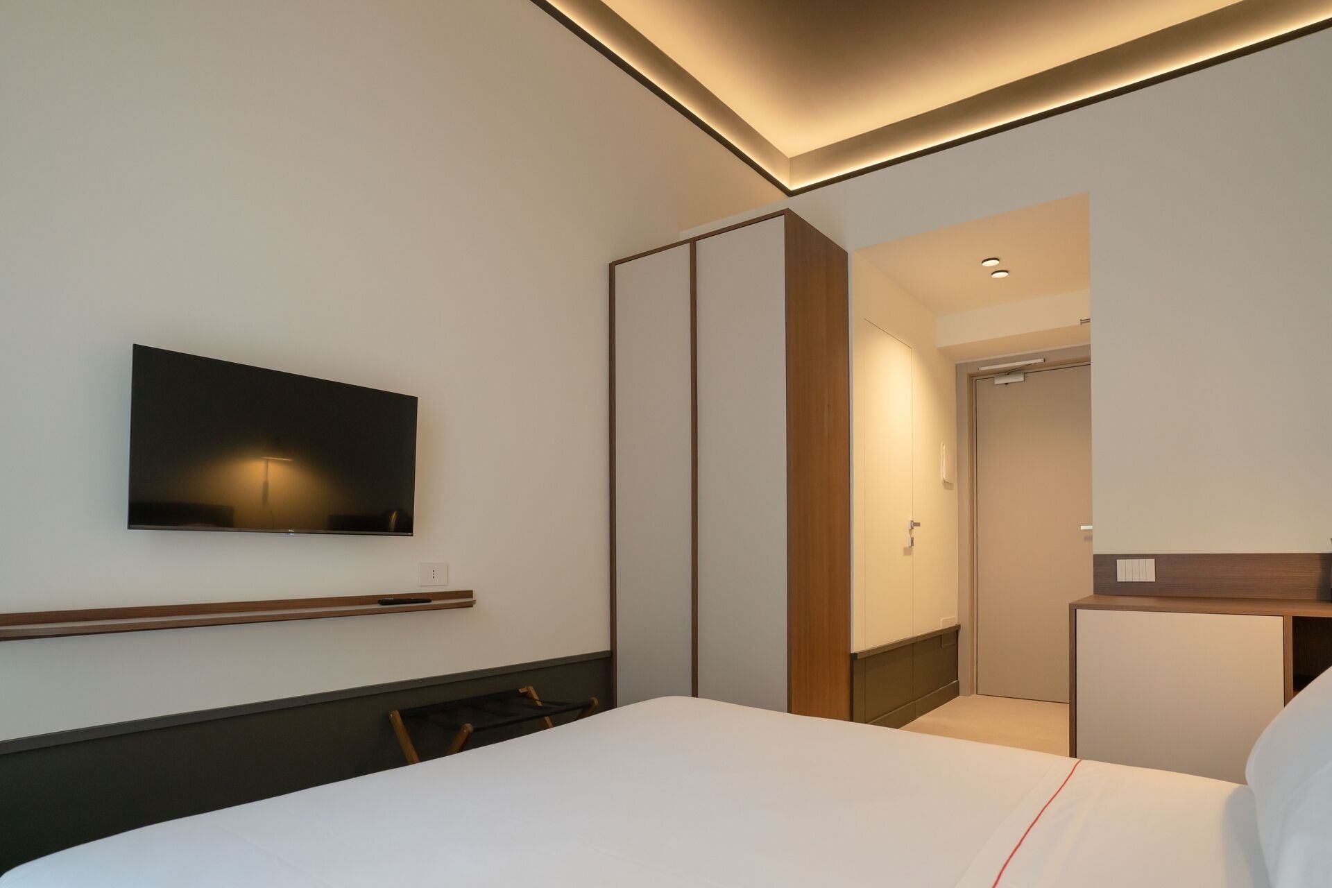 Ein modernes Hotelzimmer mit einem großen Bett, einem flachbildfernseher an der Wand, einem Kleiderschrank mit Schiebetüren und einem kleinen Nachttisch.