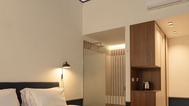 A modern hotel room with a large bed, a bedside lamp, a built-in wardrobe, and a shower area. - Maison Petronilla (Naples)