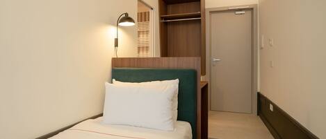 A hotel room with a bed, a bedside lamp, a wardrobe, and an air conditioning unit.
