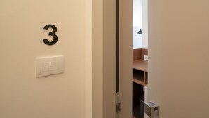 A door with the number 3 on the wall, a light switch, and a partially open door revealing a room with a wooden shelf. - Maison Petronilla (Naples)