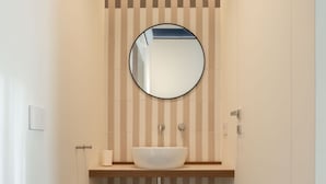 A narrow bathroom with a round mirror, a white sink, and striped walls. - Maison Petronilla (Naples)