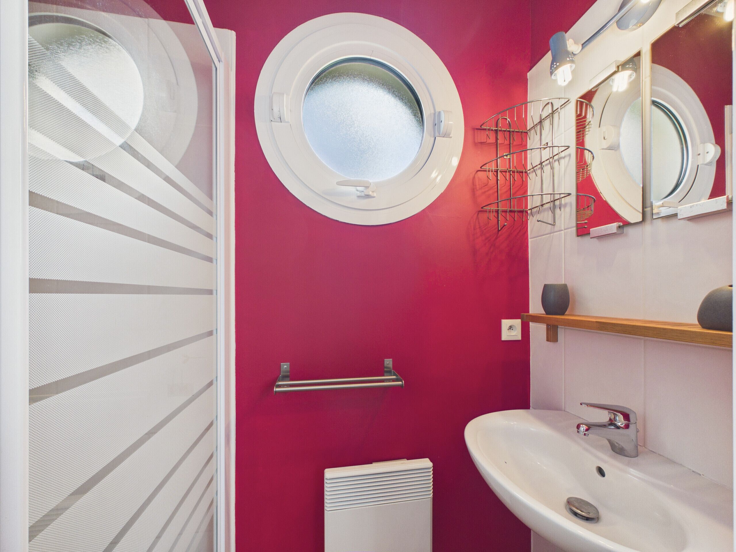 A bathroom with a red wall, a round window, a white sink, and a mirror.