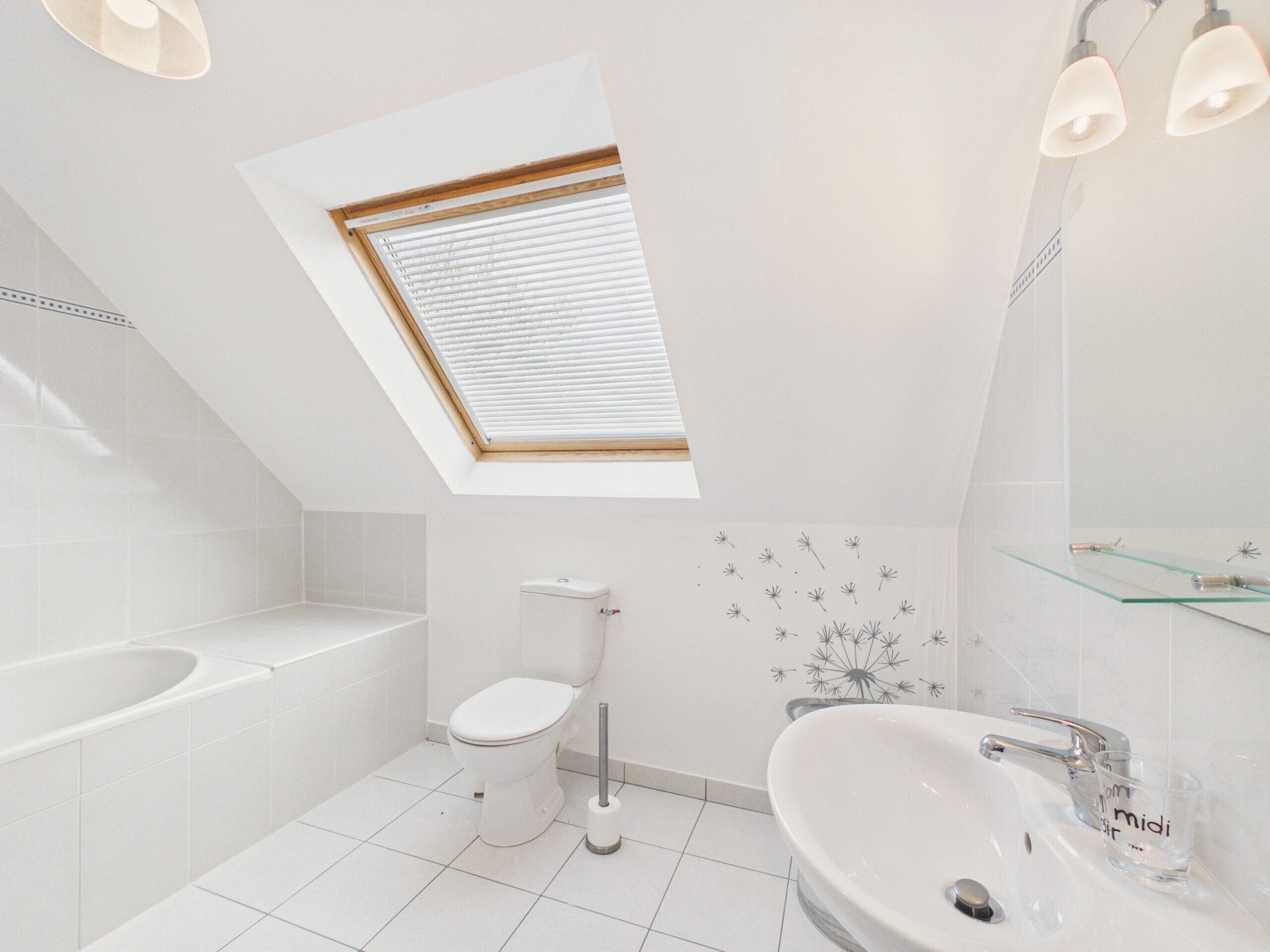 A modern bathroom with a skylight, a bathtub, a toilet, and a sink with a glass shelf.