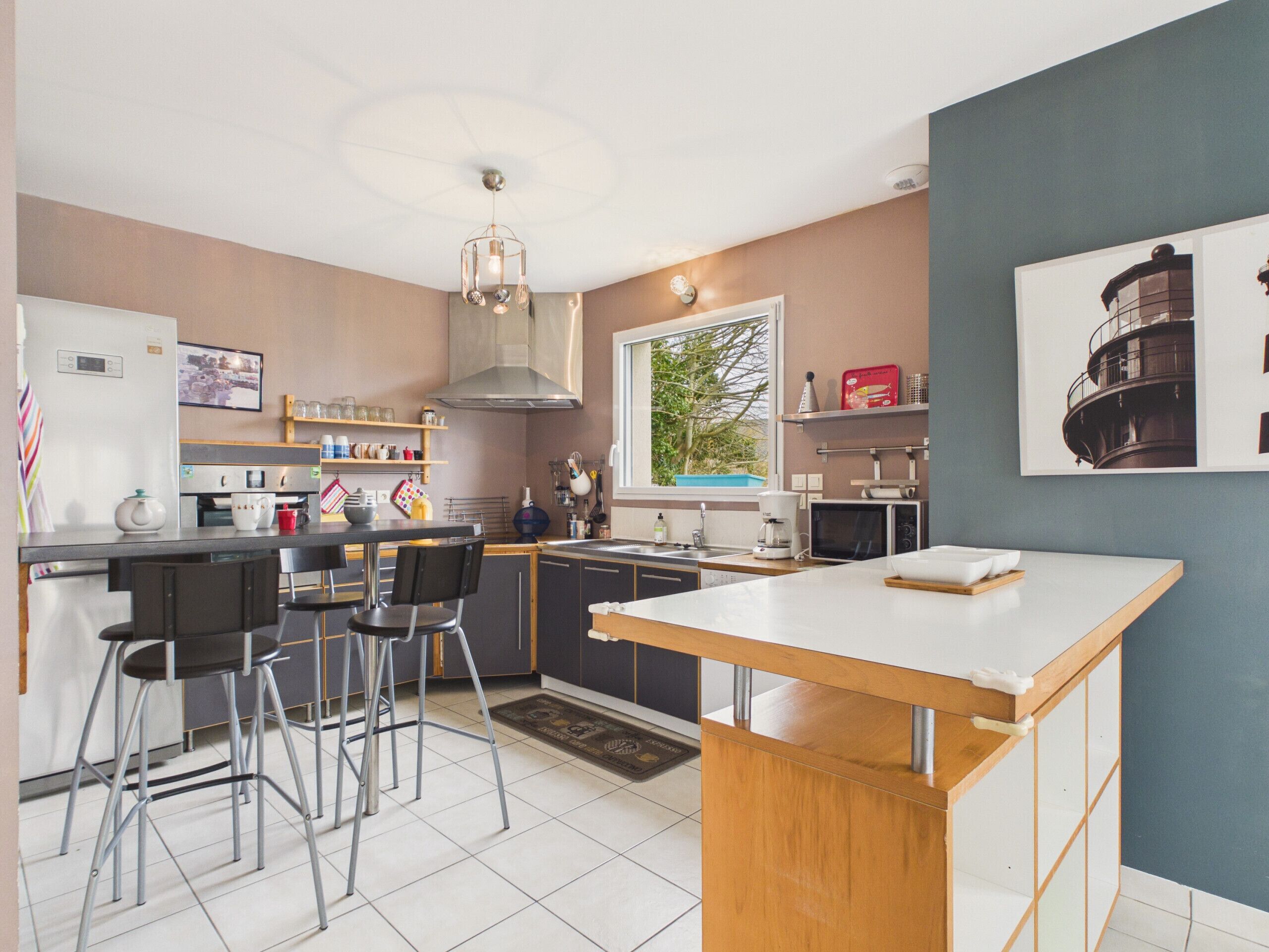 A modern kitchen with a central island, bar stools, a built-in oven, and a window with a view of greenery.