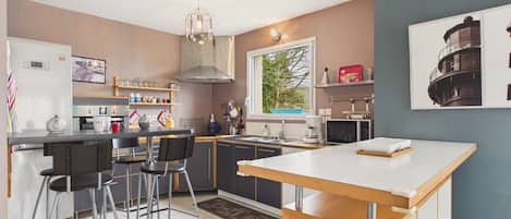 A modern kitchen with a central island, bar stools, a built-in oven, and a window with a view of greenery.