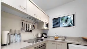A modern kitchen with a built-in oven, microwave, and sink. There is a window with blinds, and various kitchen utensils are visible.