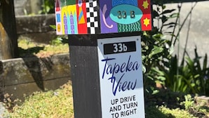 A colorful birdhouse with a house number sign below it.