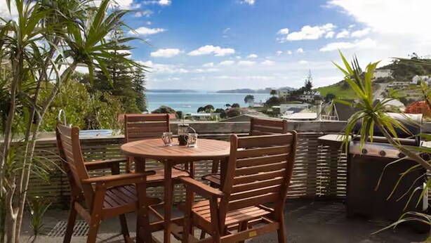 A wooden table and chairs with a view of the sea and a distant town.