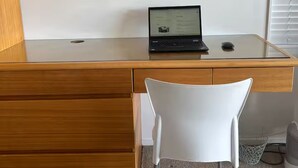 A wooden desk with a laptop, a framed map on the wall, and a white chair in front.