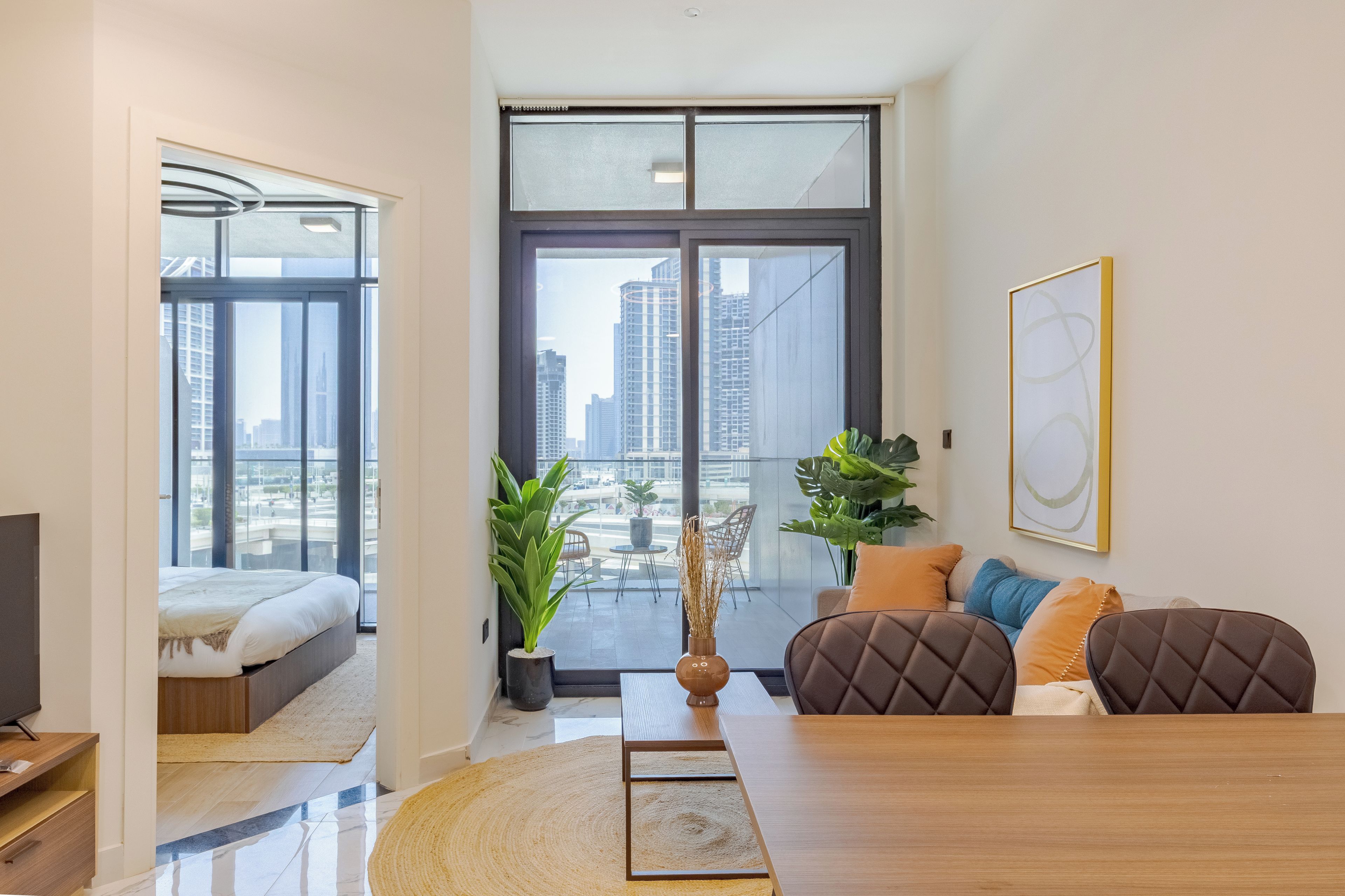 A modern living room with a large window, a sofa set, a dining table, and a television.