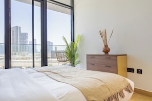 Ein Schlafzimmer mit großem Fenster, einem Bett, einem Sessel, einer Pflanze und einem Nachttisch.