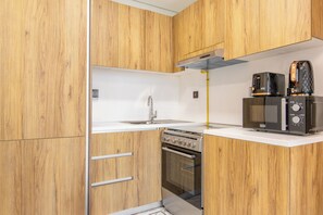 Eine kleine Küche mit Holzschränken, einer Edelstahl-Spüle, einem Herd und einem schwarzen Toaster.