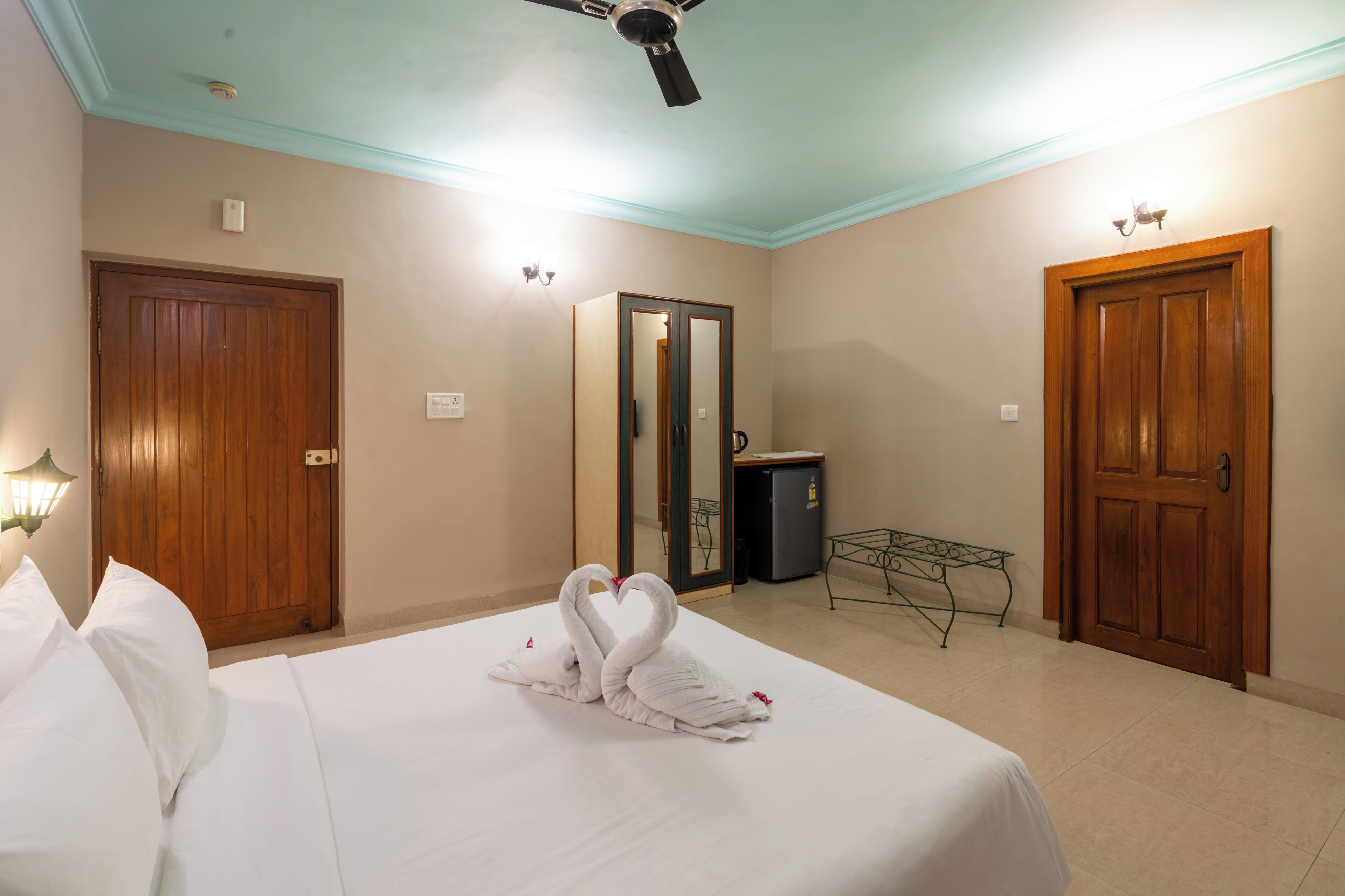 A hotel room with a bed, a ceiling fan, a mirror, a desk, and a wardrobe.