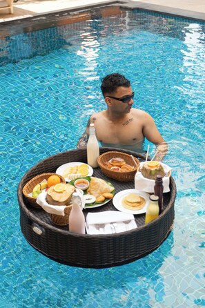 A person in a pool with a floating tray containing food and drinks. - Victor Exotica an Indy Resort (Candolim)