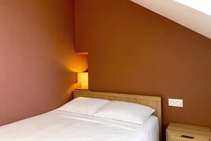 A neatly made bed with white linens in a room with brown walls and a sloped ceiling.