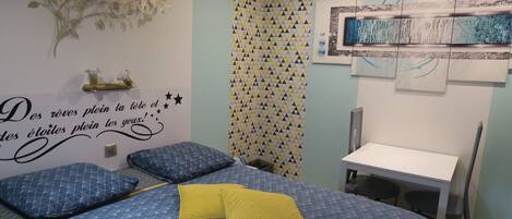 Un dormitorio con cama, escritorio y silla. Hay una pared decorativa con patrón geométrico y un adhesivo mural con texto.