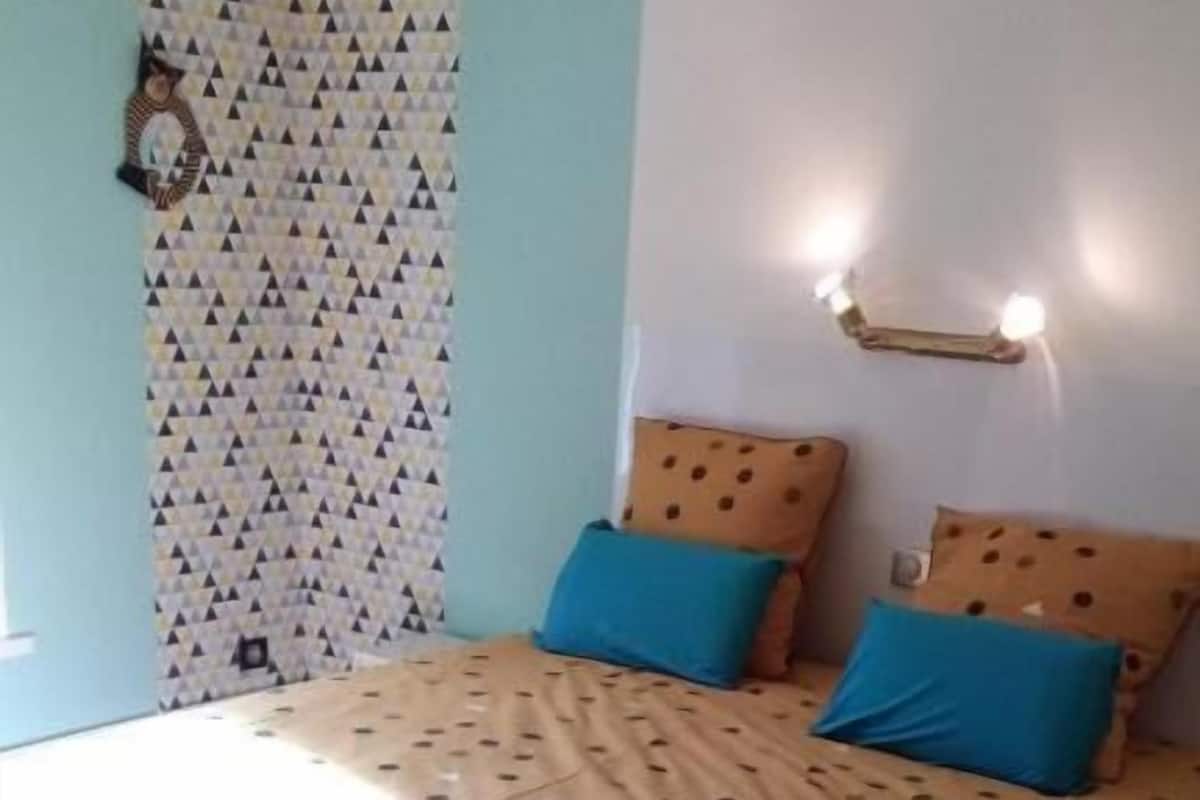 A bedroom with a bed, a nightstand, a wall-mounted light, and a patterned curtain.