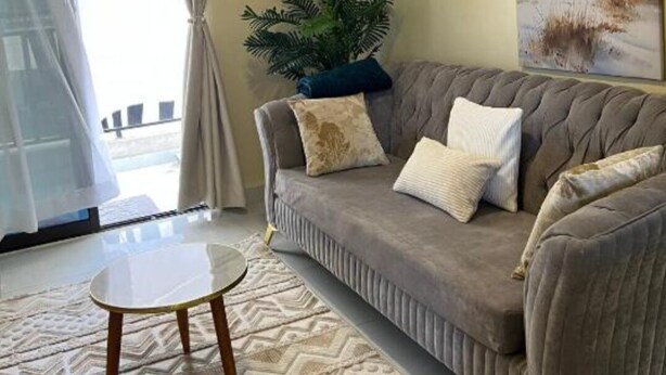 A living room with a grey sofa, a small round table, a patterned rug, a potted plant, and a painting on the wall. - Enjoyable 1-bedroom apartment perfect for a relaxing getaway (Nairobi)