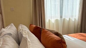 A hotel room with a bed, white and orange pillows, and sheer curtains. - Enjoyable 1-bedroom apartment perfect for a relaxing getaway (Nairobi)