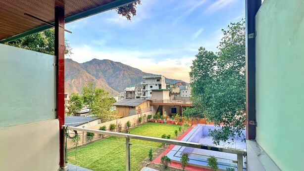 A balcony with a view of a residential area, a mountain in the background, and a clear sky. - Devora Resort (Rishikesh)
