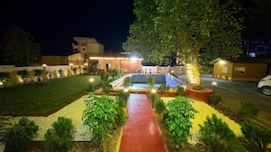 A well-lit courtyard with a swimming pool, surrounded by greenery and a paved walkway. - Devora Resort (Rishikesh)
