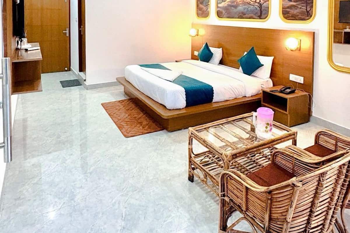 Una habitación de hotel con cama, ventilador de techo, mesita de noche, sillón y cuadros colgados en la pared.