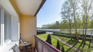 A balcony with a table and chairs, overlooking a green lawn and trees. - Comfortable Apartment in Gdansk | Balcony | Workspace (Gdańsk)