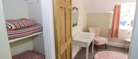 Een slaapkamer met een bed, een bureau, een stoel, een roze vloerkleed en een kledingkast met opgevouwen handdoeken.