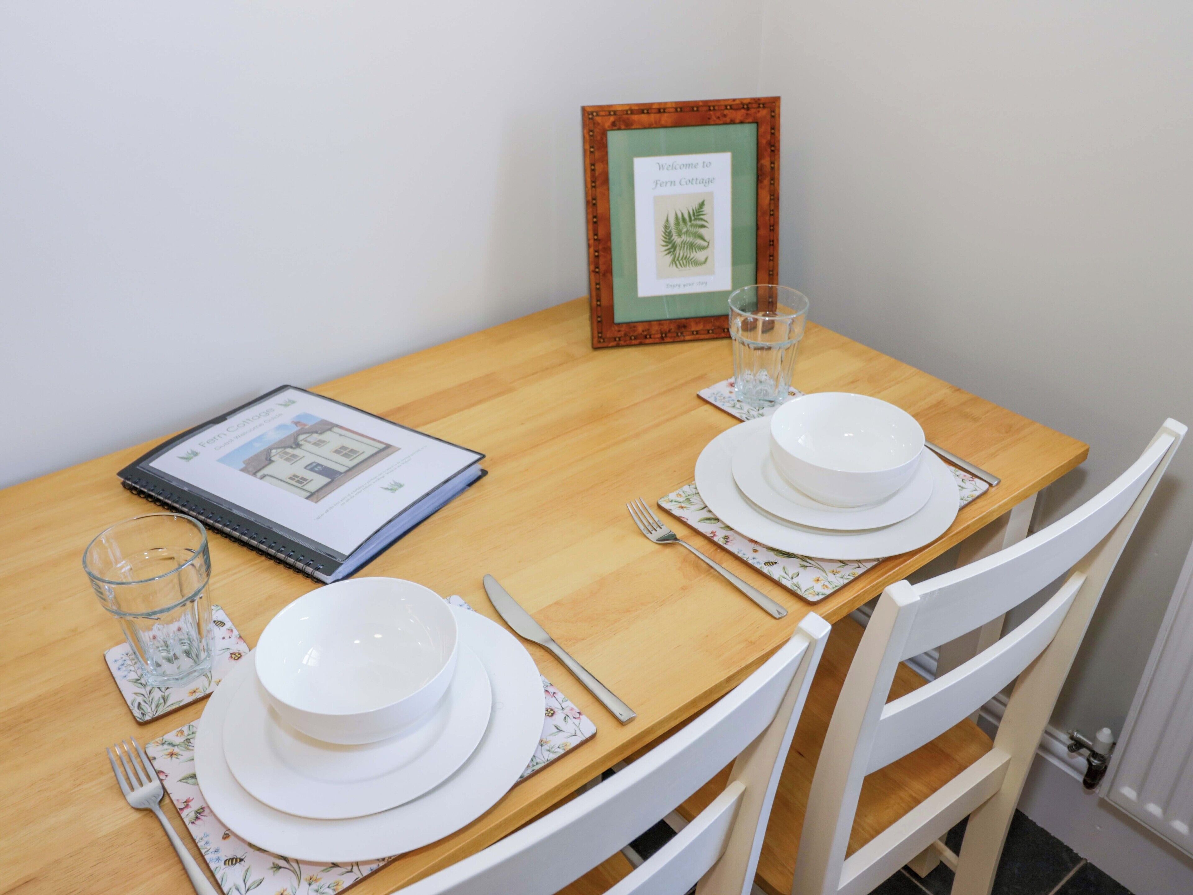Une table à manger agrémentée d’un panneau d’accueil encadré, d’un carnet, d’un verre et de couverts.