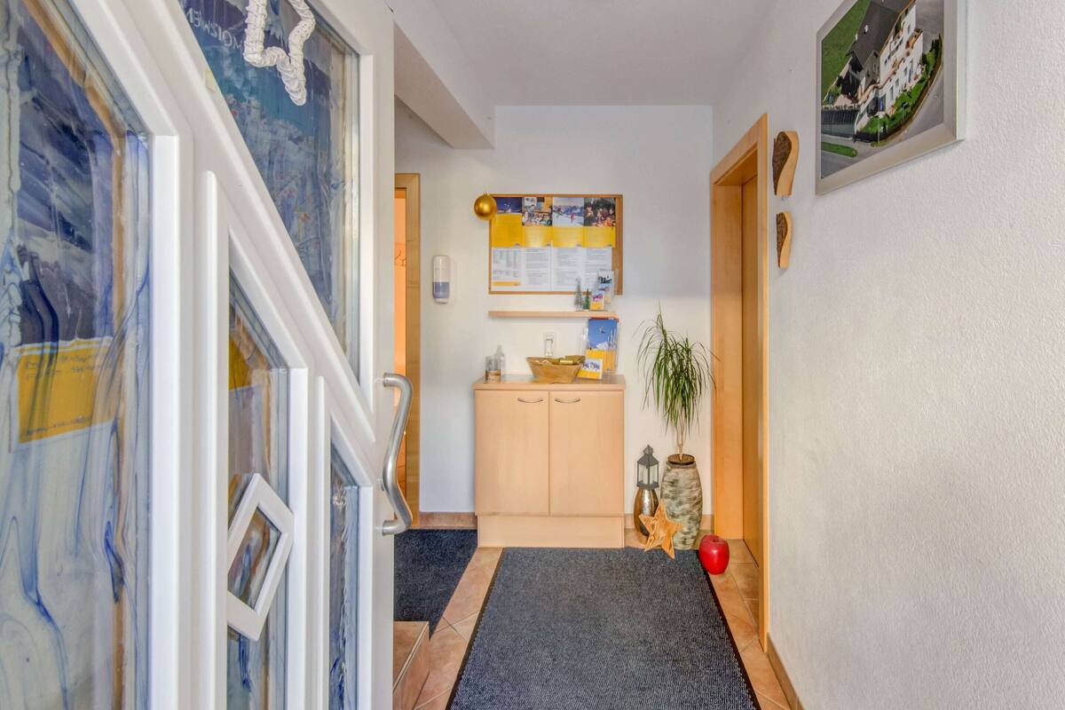Un couloir avec une armoire en bois, un tableau d’affichage, une plante en pot et une pomme rouge sur le sol.